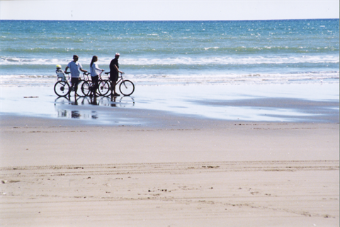 River Mouth Trail - Family walking bikes along the beach's water edge.